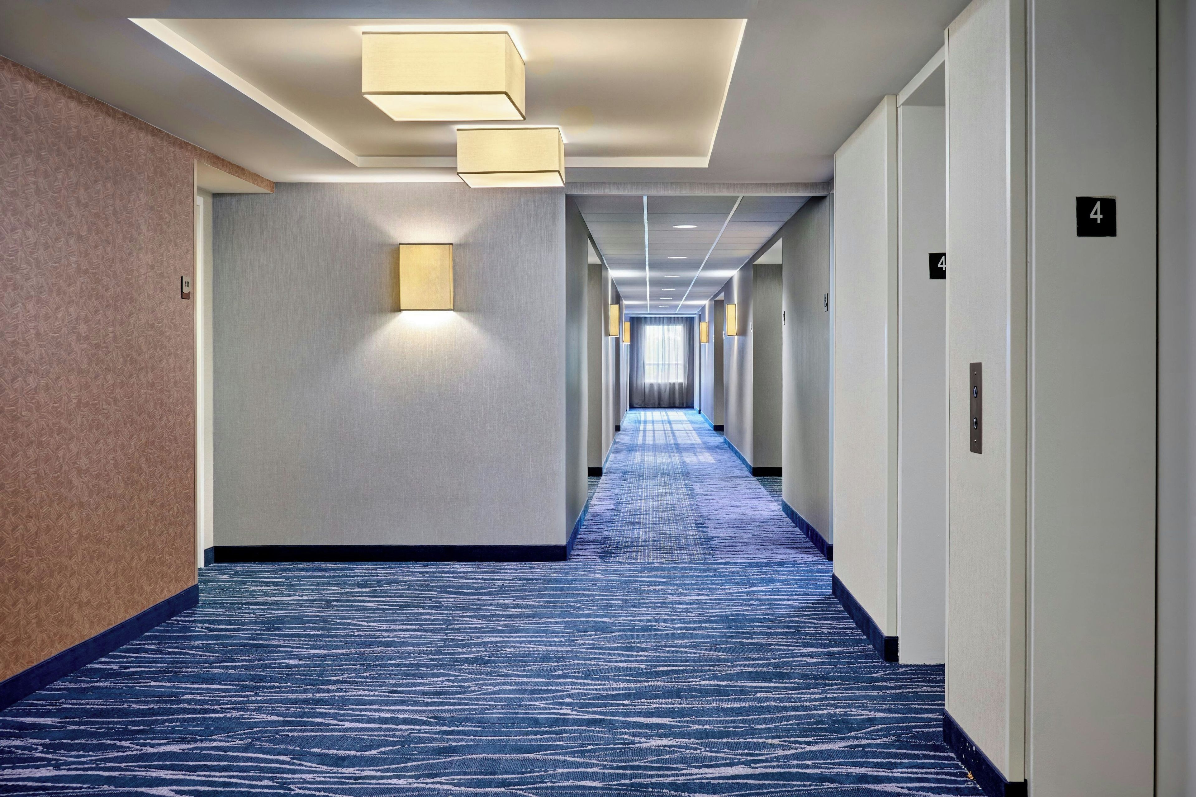 A hotel hallway with a blue carpet, light-colored walls, and a number 4 on the wall.