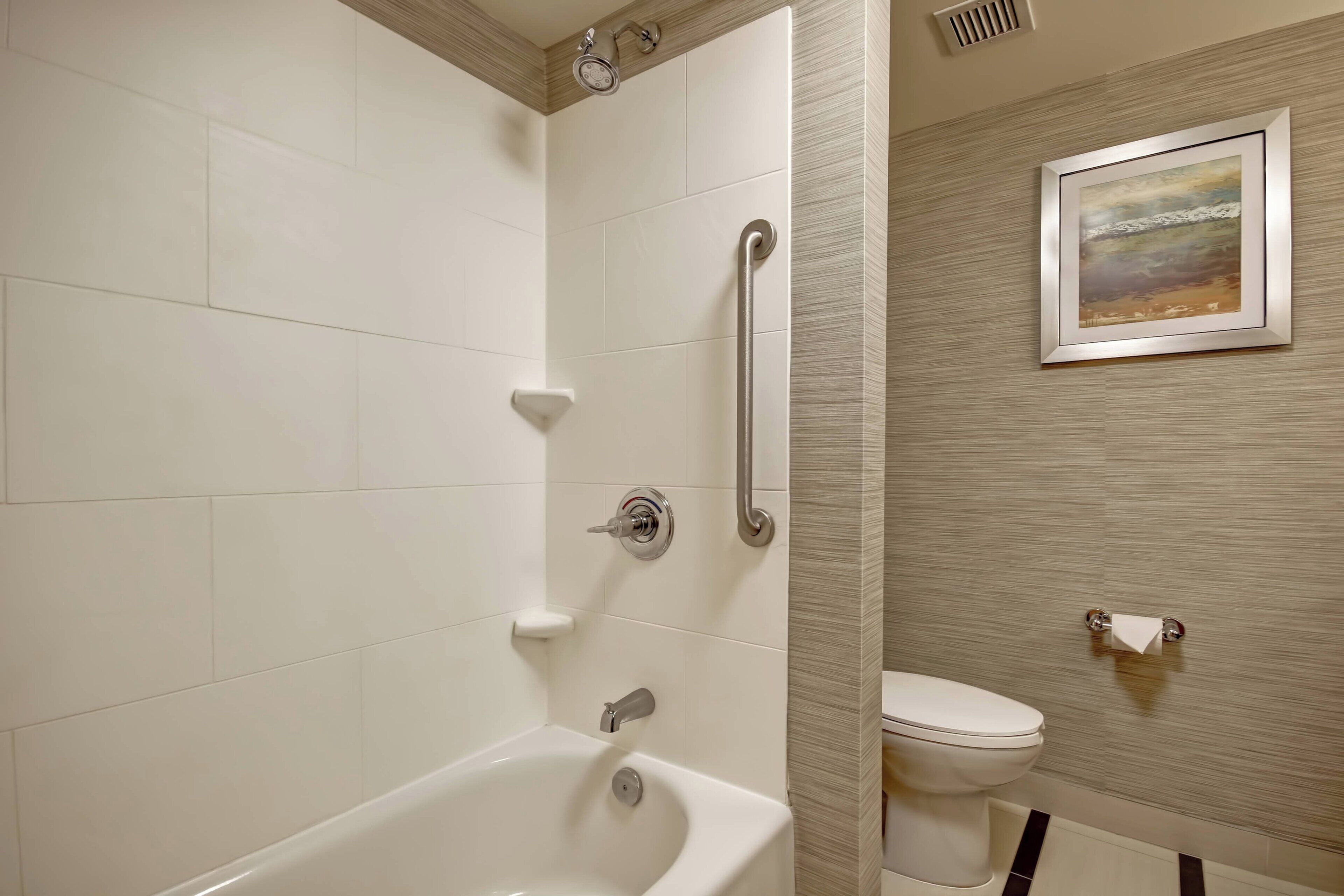 Un baño moderno con bañera, inodoro y barra de apoyo.