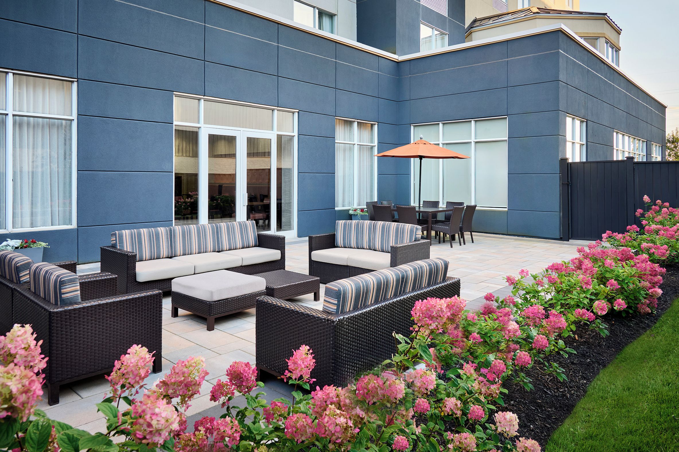 A modern outdoor patio with wicker furniture, a dining table, and a large umbrella.