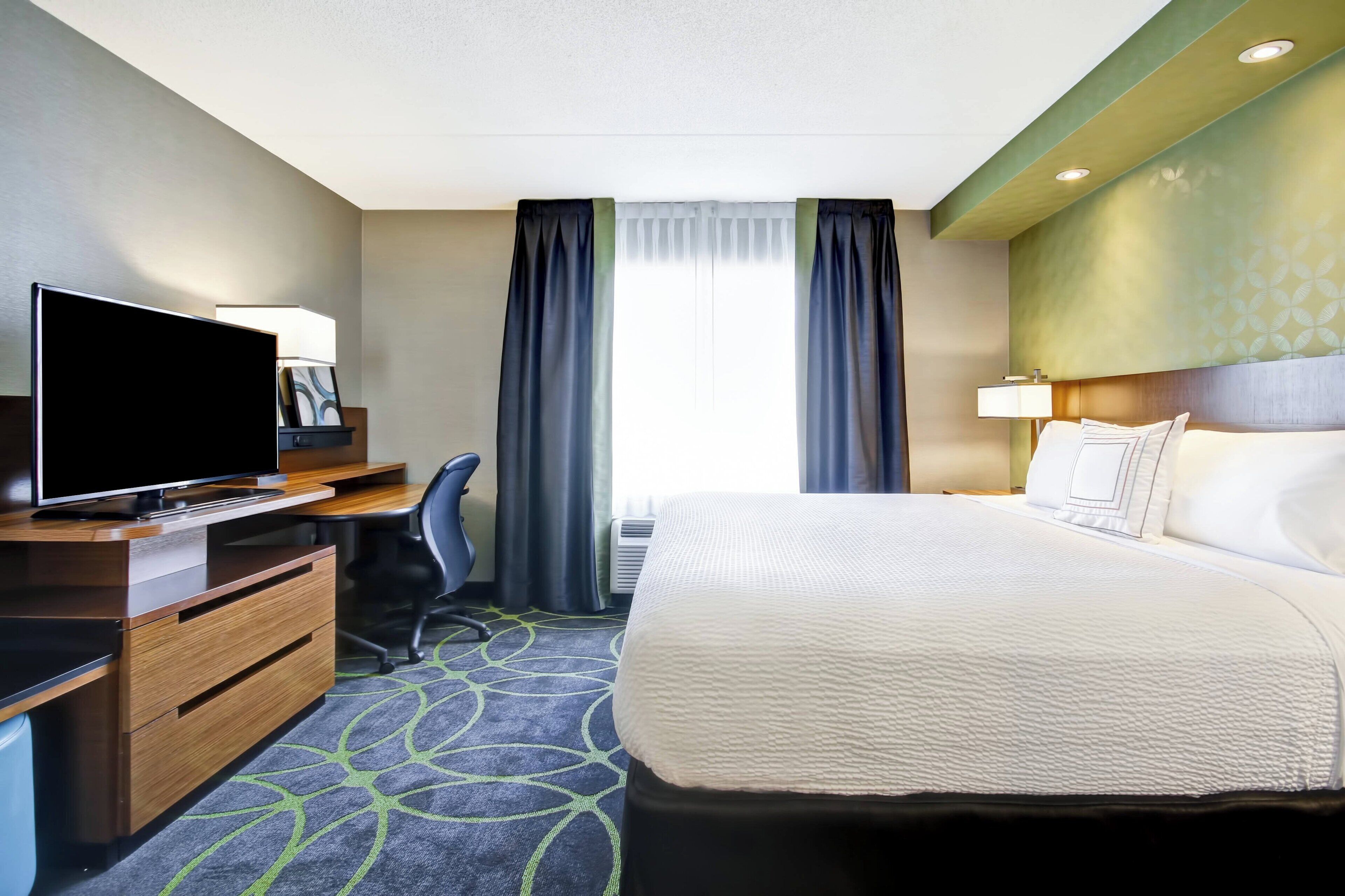 Una habitación de hotel con cama, escritorio, televisión y vistas al exterior.