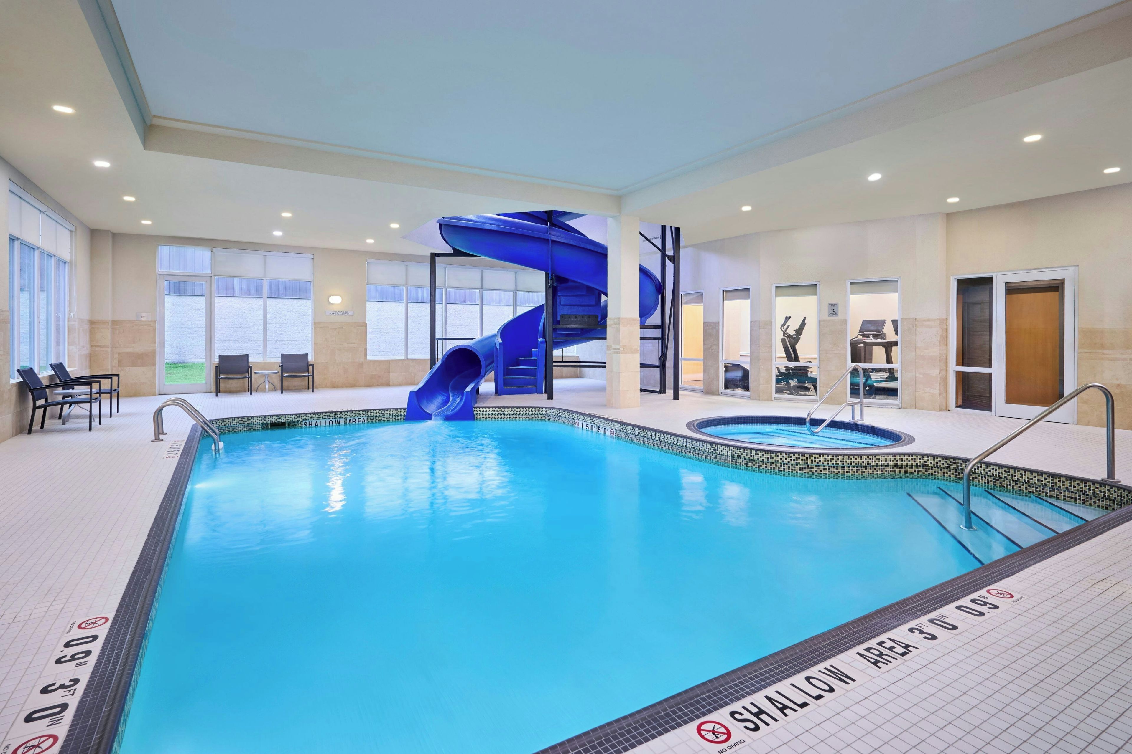 An indoor swimming pool with a blue slide, seating area, and exercise equipment.