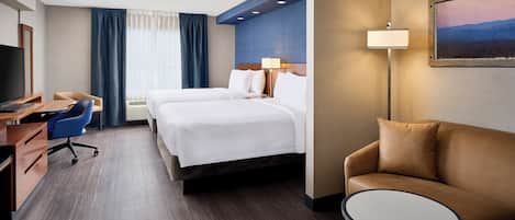 A hotel room with a bed, a desk with a chair, a sofa, and a small table.