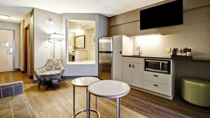 A modern kitchen with a refrigerator, microwave, and a flat-screen TV mounted on the wall.