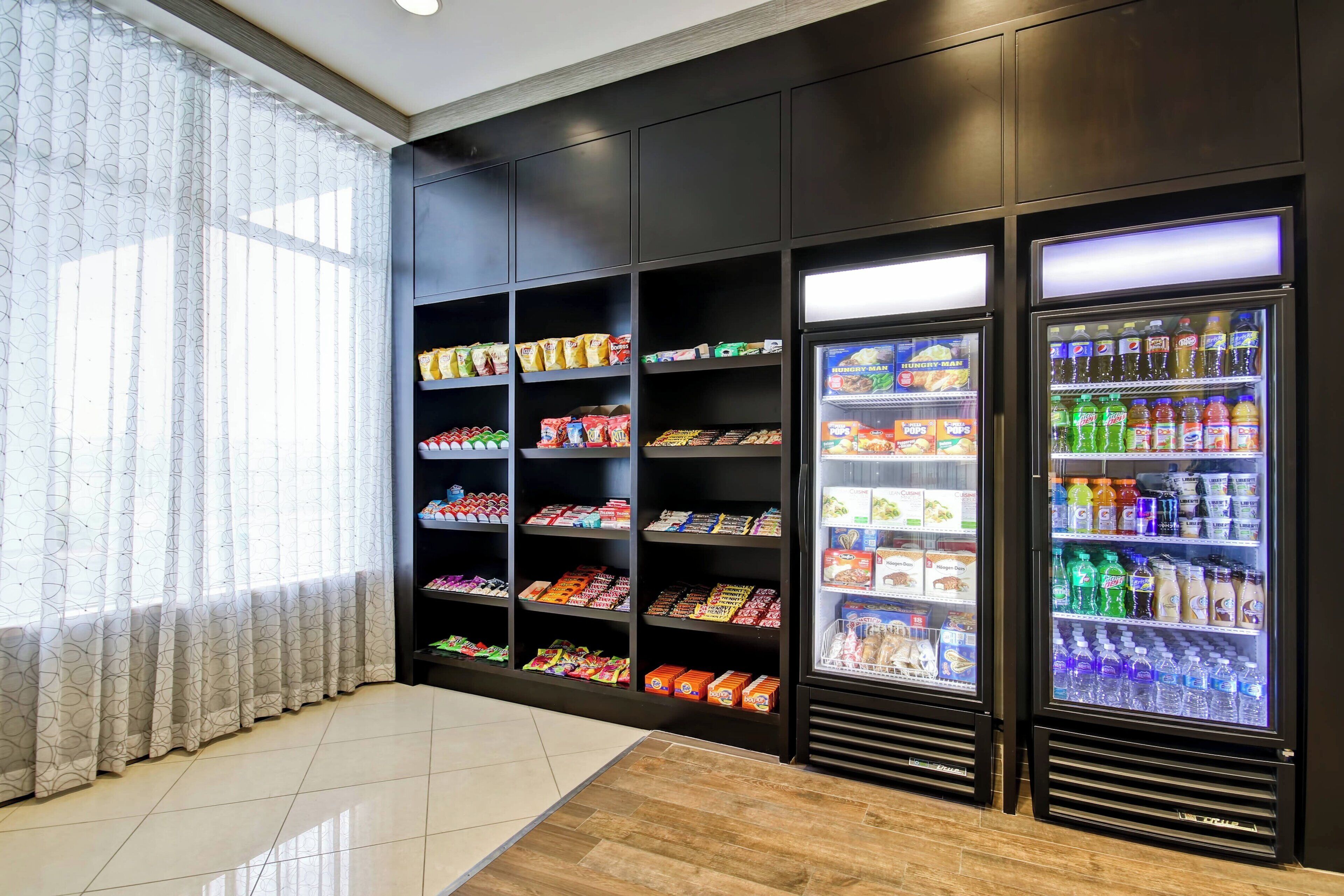 A vending area with snack and drink dispensers, shelves with packaged goods, and a window with curtains.