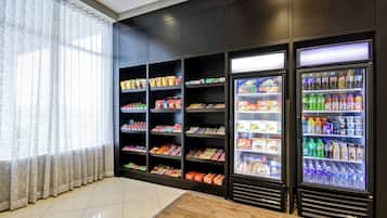 A vending area with snack and drink dispensers, shelves with packaged goods, and a window with curtains.