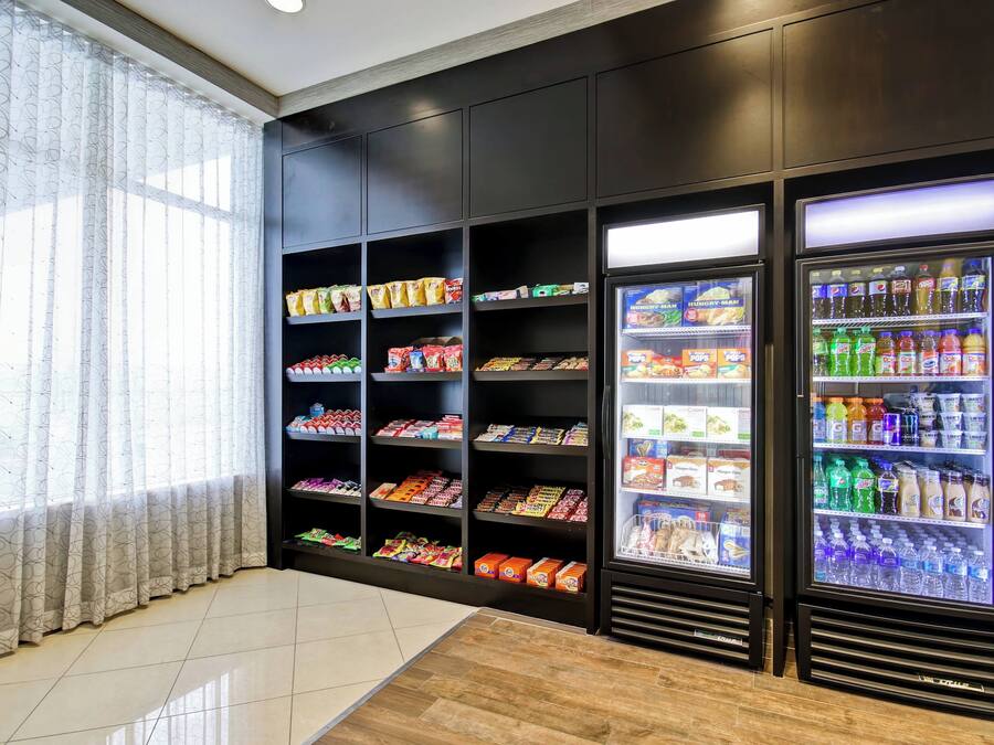 Un área de venta con máquinas expendedoras de aperitivos y bebidas, estantes con productos envasados, y un ventanal con cortinas.