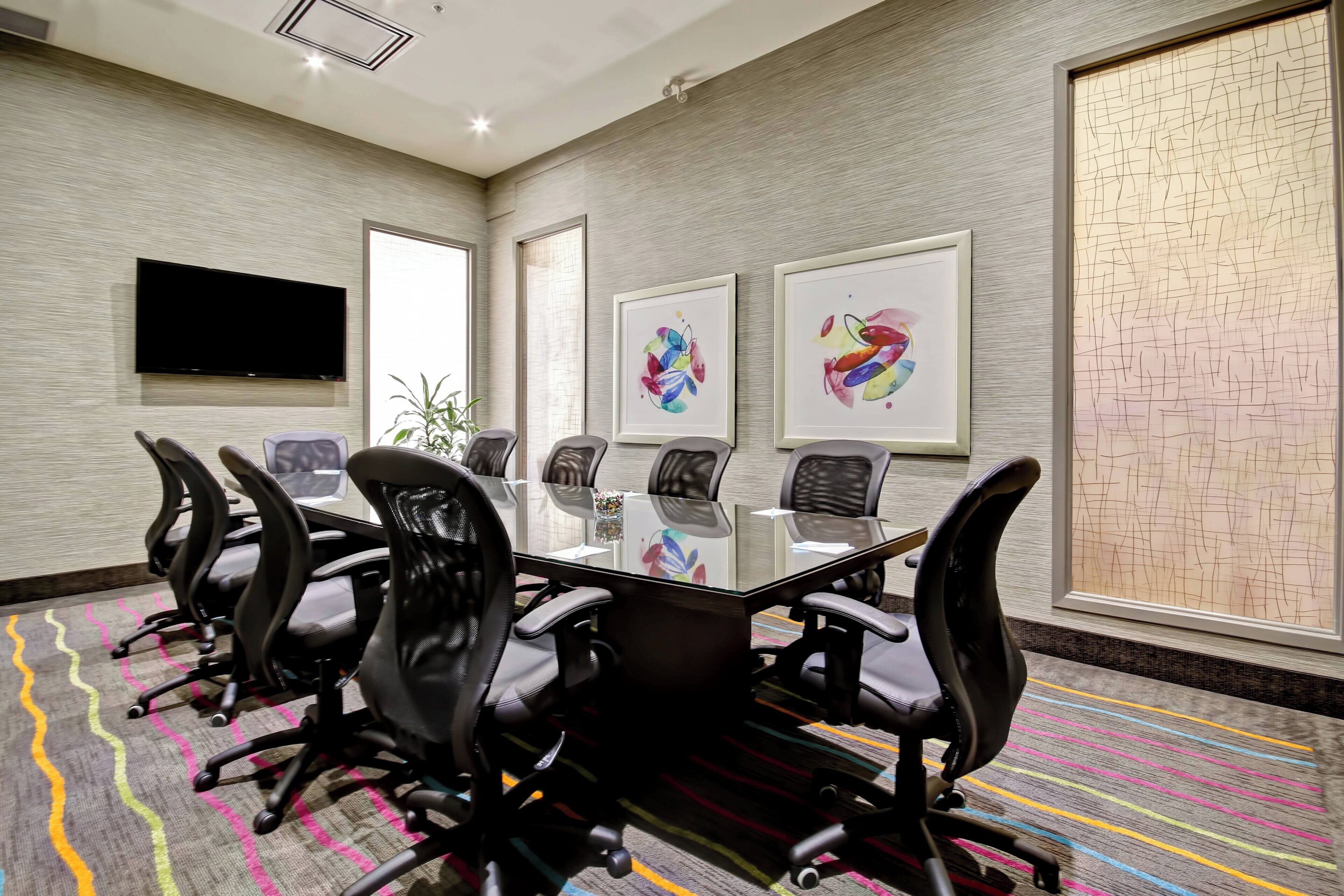 A conference room with a glass table, black chairs, a flat-screen TV, and abstract art on the walls.