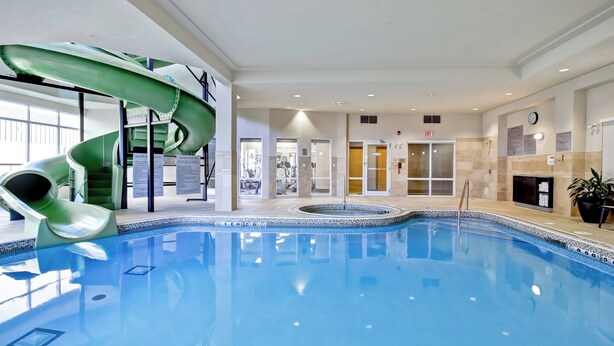 An indoor swimming pool with a green water slide, exercise area, and a fireplace.
