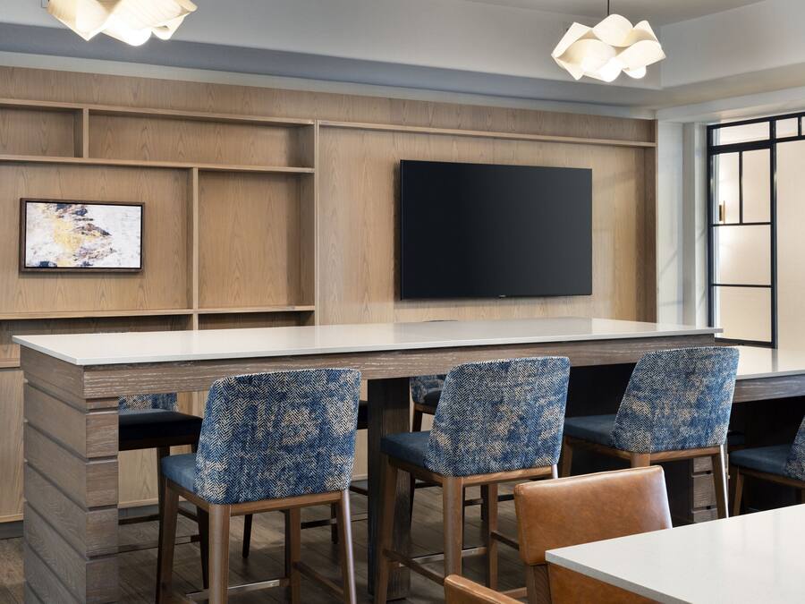 Una cocina moderna con armarios de madera, un televisor de pantalla plana grande montado en la pared y asientos de bar con sillas estampadas.