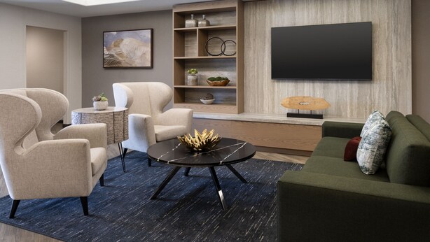 Ein modernes Wohnzimmer mit einer Couch, Sesseln, einem Couchtisch und einem an der Wand befestigten Fernseher.