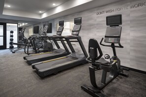 Een sportschool met loopbanden, elliptische trainers en een muur met motiverende tekst.