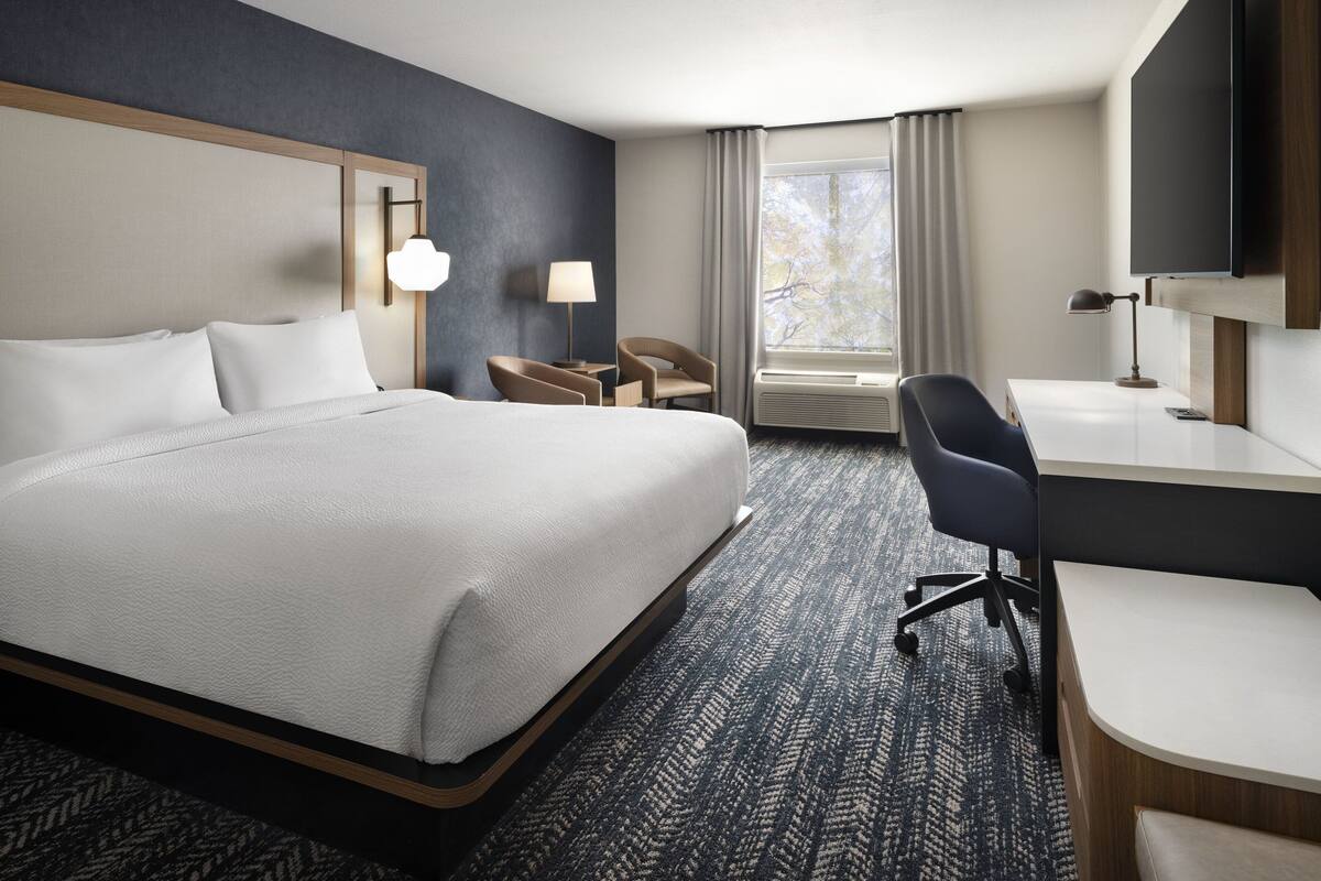 Une chambre d’hôtel avec un grand lit, un bureau, une chaise, une télévision et une fenêtre avec des rideaux.
