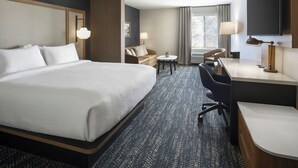 Ein Hotelzimmer mit einem großen Bett, einem Schreibtisch, einem Sessel, einem kleinen Tisch und einem Fernseher.