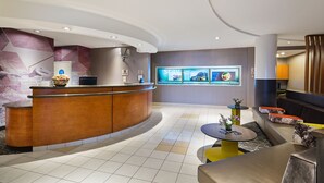 A modern hotel lobby with a curved reception desk, a seating area with sofas and a coffee table, and a digital display wall. - SpringHill Suites by Marriott Denver Airport (Denver)