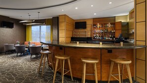 A bar area with stools, a TV, and a bar stocked with bottles. - SpringHill Suites by Marriott Denver Airport (Denver)