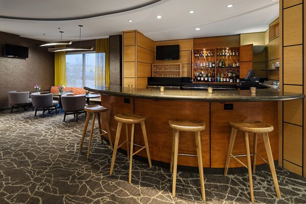 A bar area with stools, a TV, and a bar stocked with bottles. - SpringHill Suites by Marriott Denver Airport (Denver)