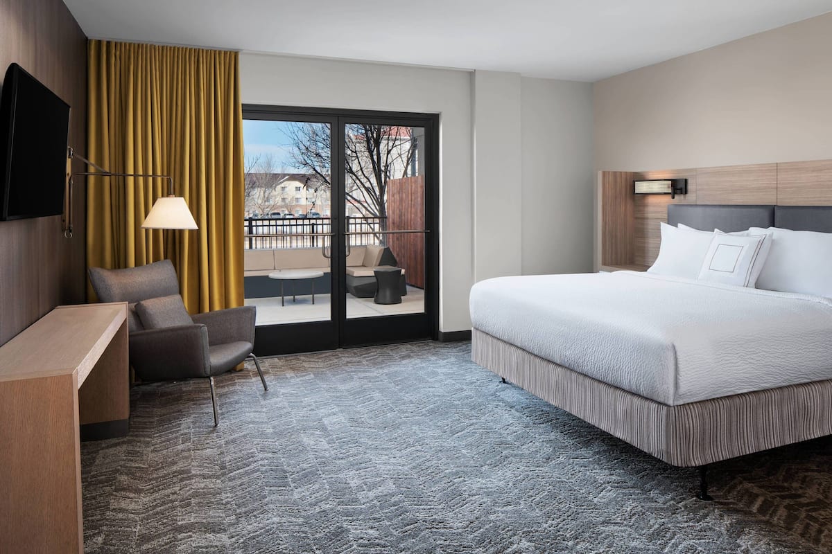 A hotel room with a large bed, a desk, a chair, a TV, and a view of the outdoors through a sliding door.