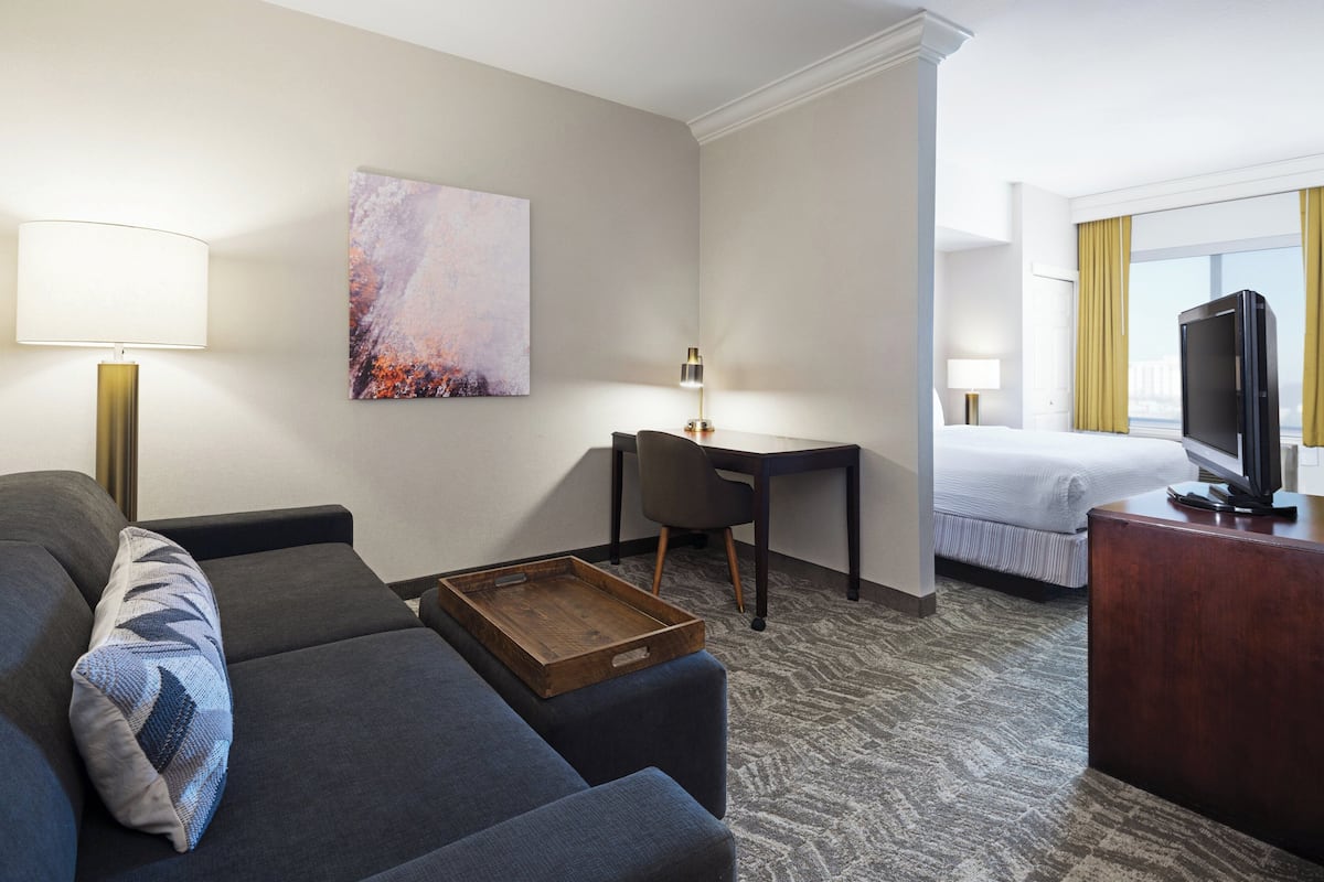 A hotel room with a sofa, a desk, a bed, a television, and a painting on the wall.