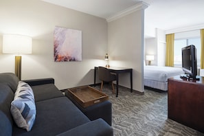 Een hotelkamer met een bank, bureau, bed, televisie en een schilderij aan de muur.