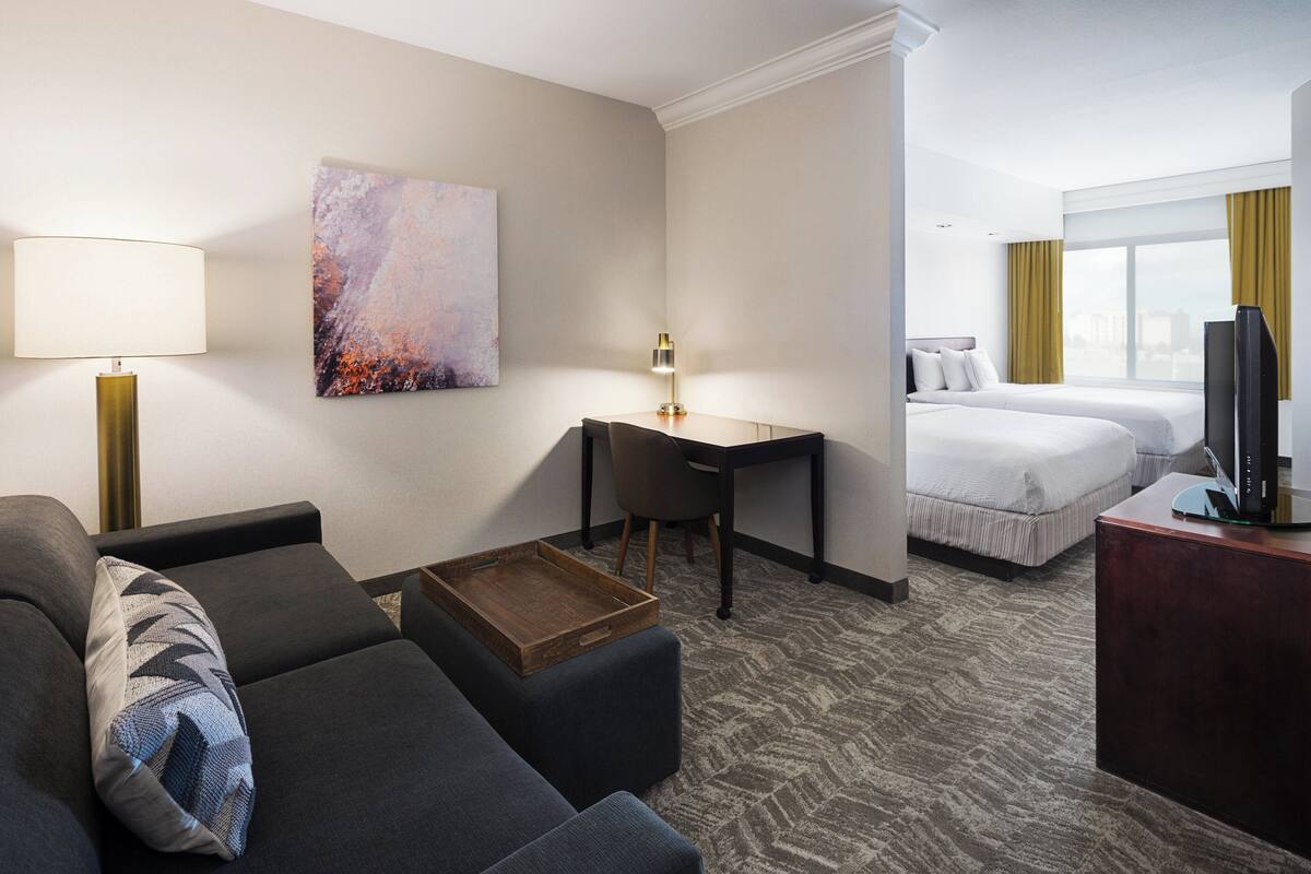 A hotel room with a sofa, a desk, a bed, and a television.