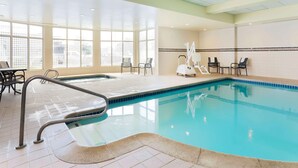 An indoor swimming pool with clear glass walls, a tiled floor, and a few chairs and tables around the pool area. - Hilton Garden Inn Reno (Reno)