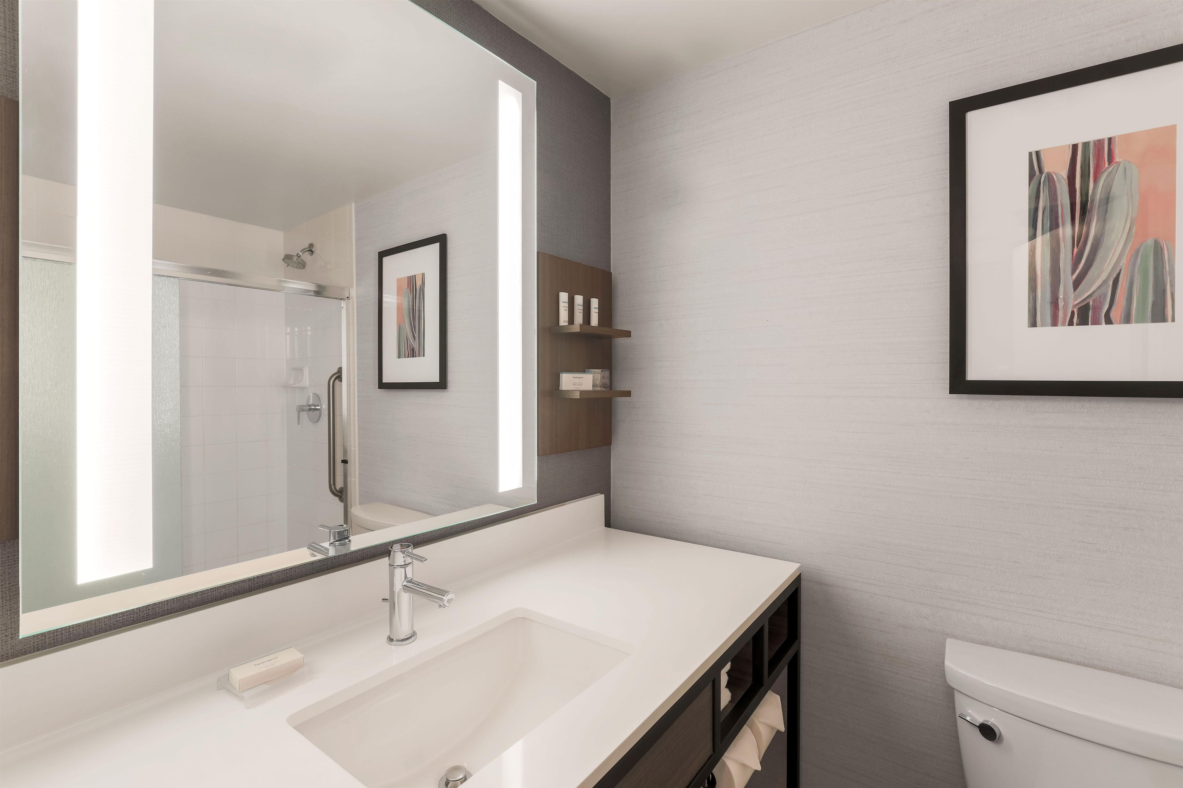 Un baño moderno con un espejo grande, un lavamanos, un inodoro y una ducha.