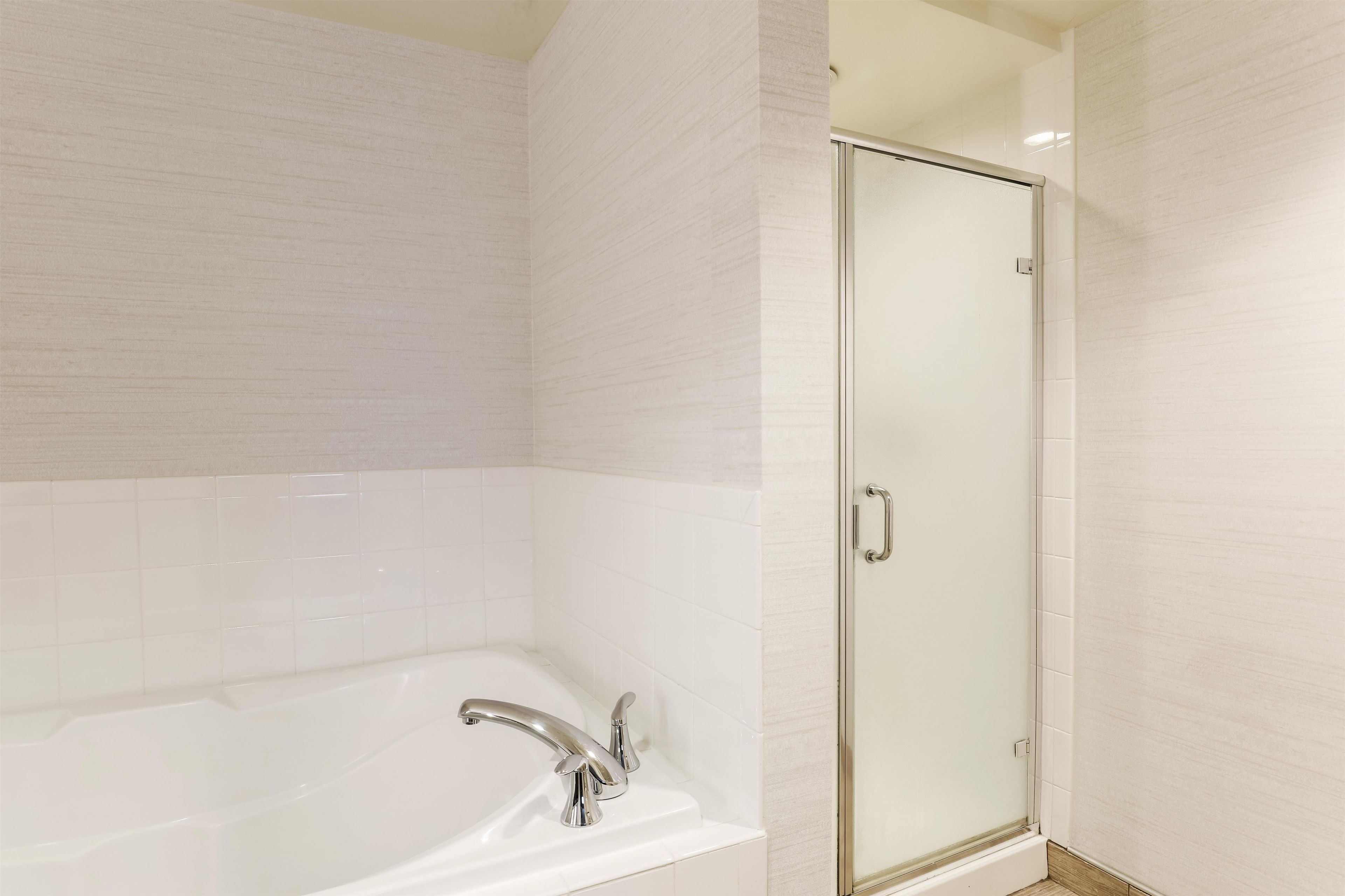 A bathroom with a bathtub, a glass shower enclosure, and white tiled walls.