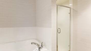 A bathroom with a bathtub, a glass shower enclosure, and white tiled walls.