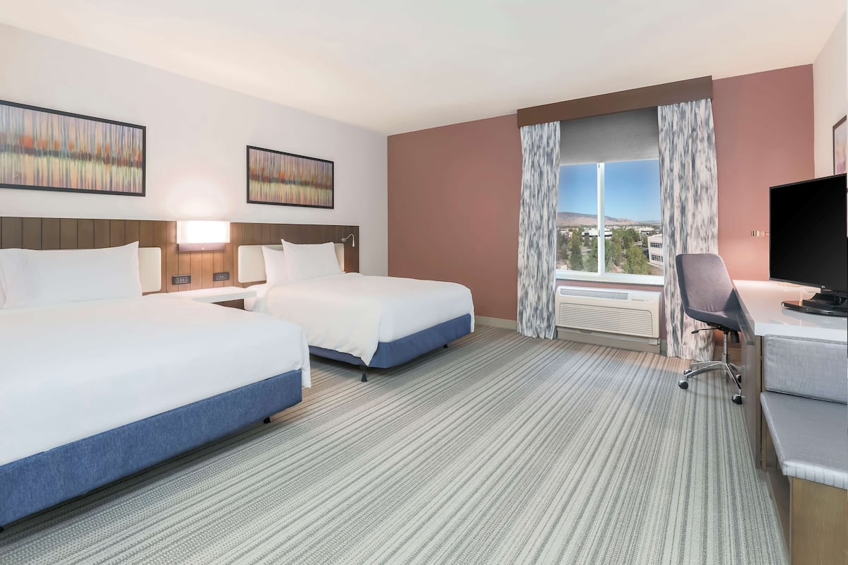 A hotel room with two beds, a desk, a chair, a TV, and a window with a view.
