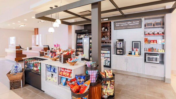 A modern coffee shop with a counter displaying snacks and beverages, a refrigerated section with chilled drinks, and a coffee machine. - Hilton Garden Inn Reno (Reno)