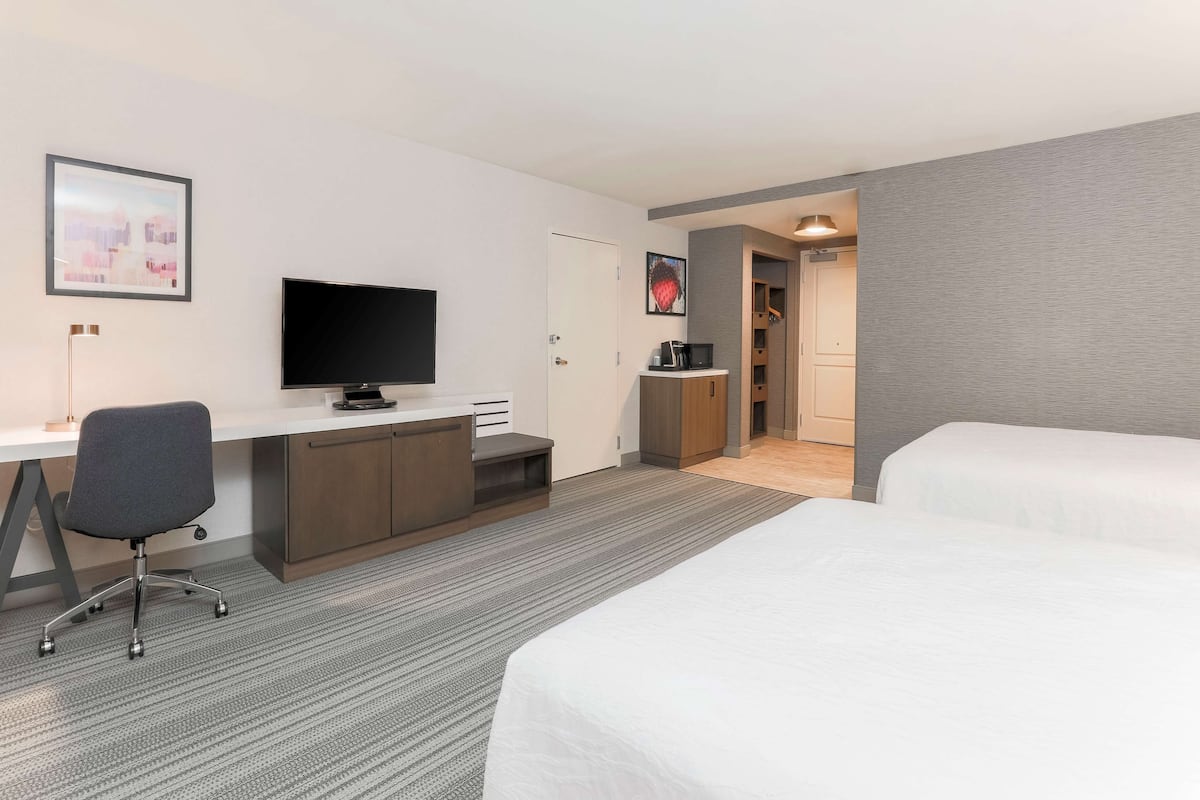 A hotel room with a bed, a desk with a computer, a chair, a TV, and a microwave.