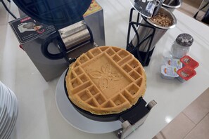 Un appareil à gaufres avec une gaufre sur une assiette, un salier et divers condiments sur un comptoir.