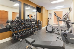 Een sportschool met fitnessapparatuur, waaronder gewichten, loopbanden en een trainingsbank.