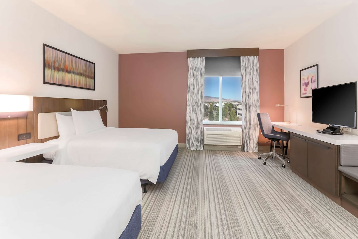 A hotel room with two beds, a desk, a TV, and a large window with a view.