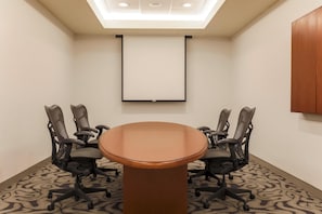 Een vergaderzaal met een ronde tafel, zes stoelen, een projectiescherm en een kamerbreed tapijt met dessin.