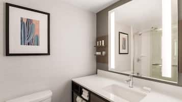 A modern bathroom with a white sink, a large mirror, and a framed abstract painting on the wall.
