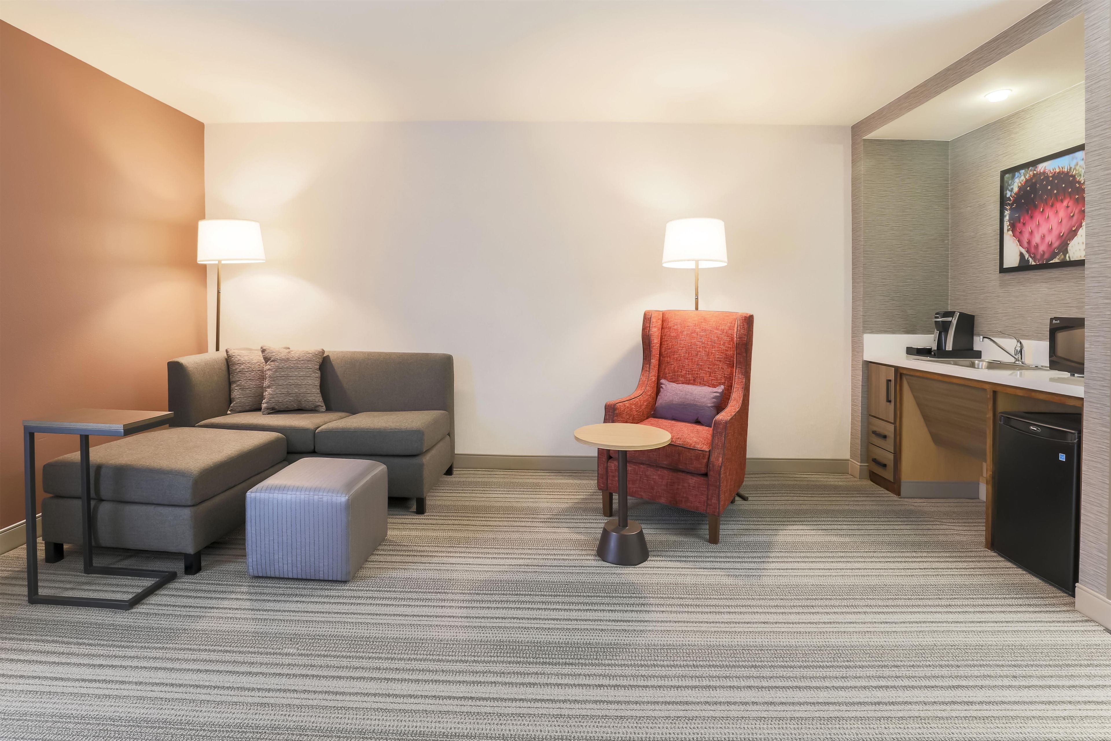 Une chambre d’hôtel équipée d’un canapé, d’un fauteuil, d’une petite table et d’une kitchenette.