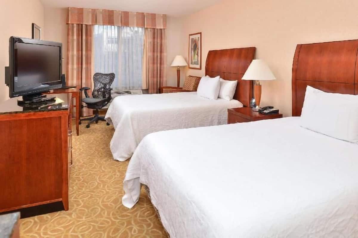 A hotel room with two beds, a television, a desk, and a chair.
