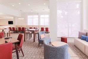 A modern hotel lobby with multiple seating areas, including a mix of tables and chairs, a sofa, and a small round table.