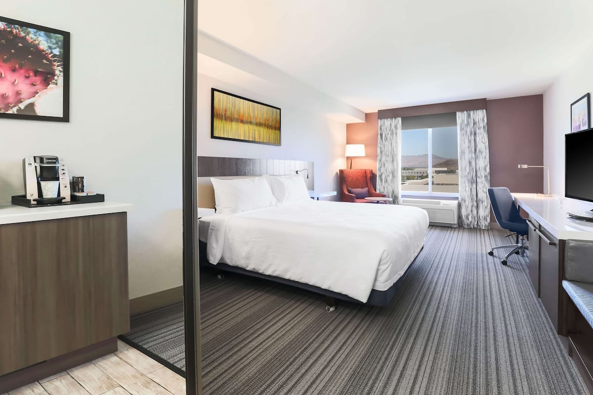 A hotel room with a bed, desk, chair, and a large window with curtains.