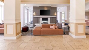 A spacious living area with a large sofa, a fireplace, and a flat-screen TV mounted above it. - Hilton Garden Inn Reno (Reno)