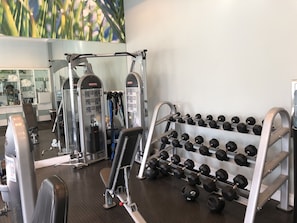 Ett gym med olika träningsmaskiner, ett ställ med hantlar och en spegel som reflekterar utrustningen.