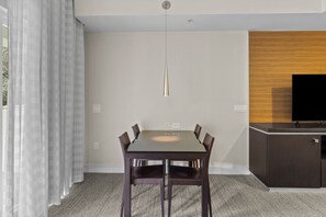 Un espace repas moderne avec une table rectangulaire et six chaises, un luminaire suspendu et un téléviseur posé sur un meuble en bois.