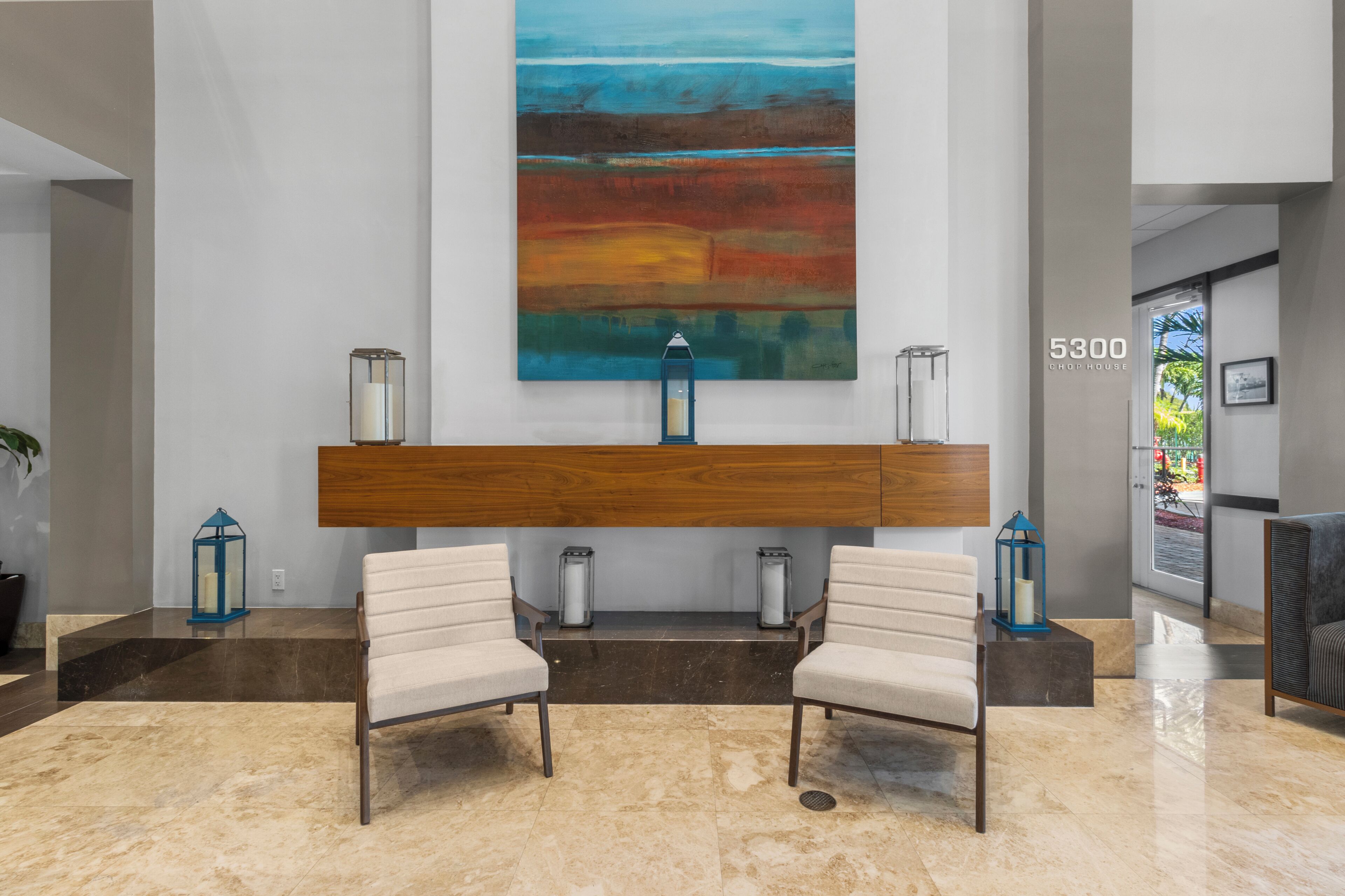 A lobby with a modern reception desk, two armchairs, and a large abstract painting on the wall.
