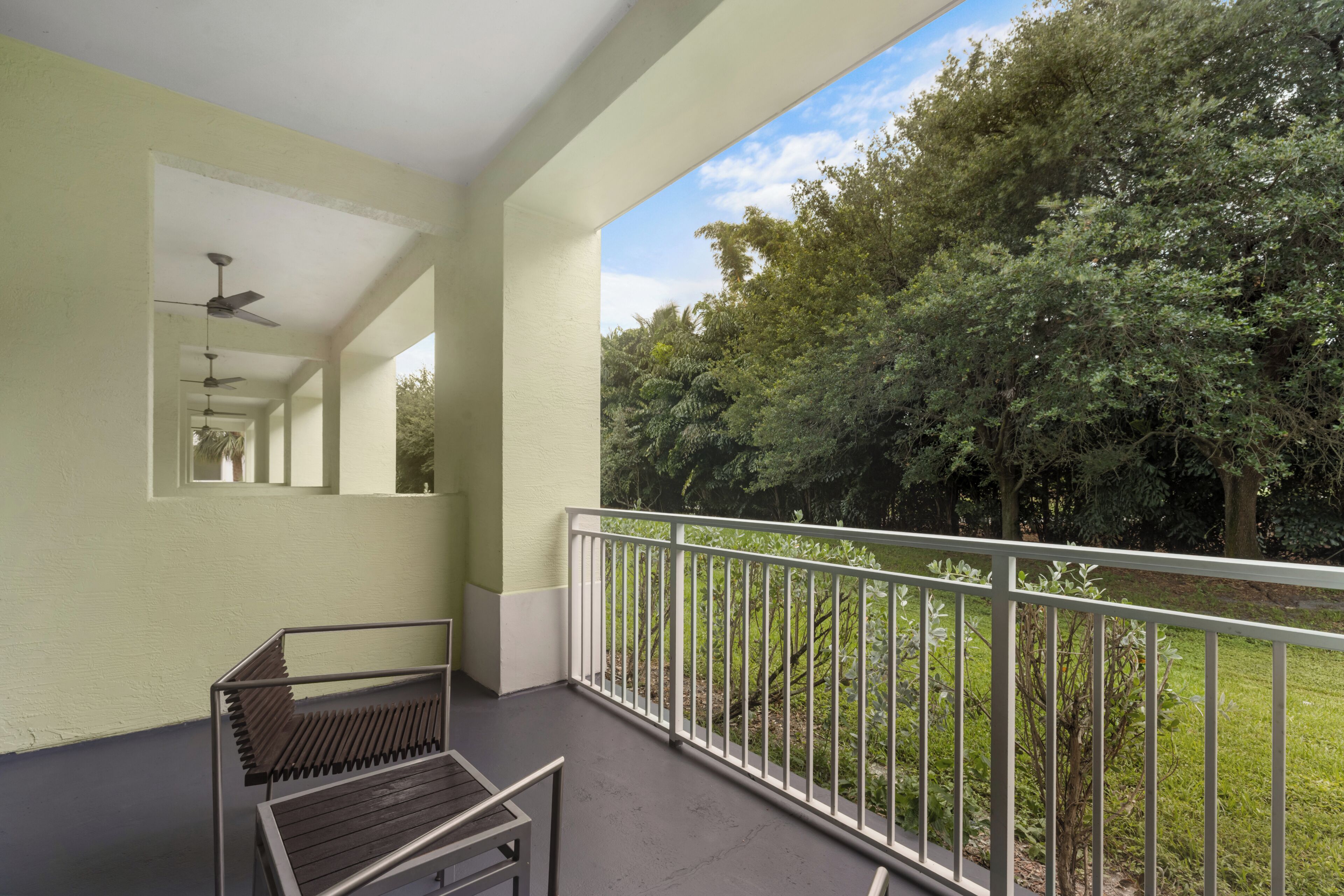 A balcony with a metal railing, a ceiling fan, and a view of dense trees.