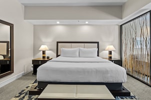A hotel room with a large bed, two bedside tables with lamps, a large mirror, and a decorative wall panel.