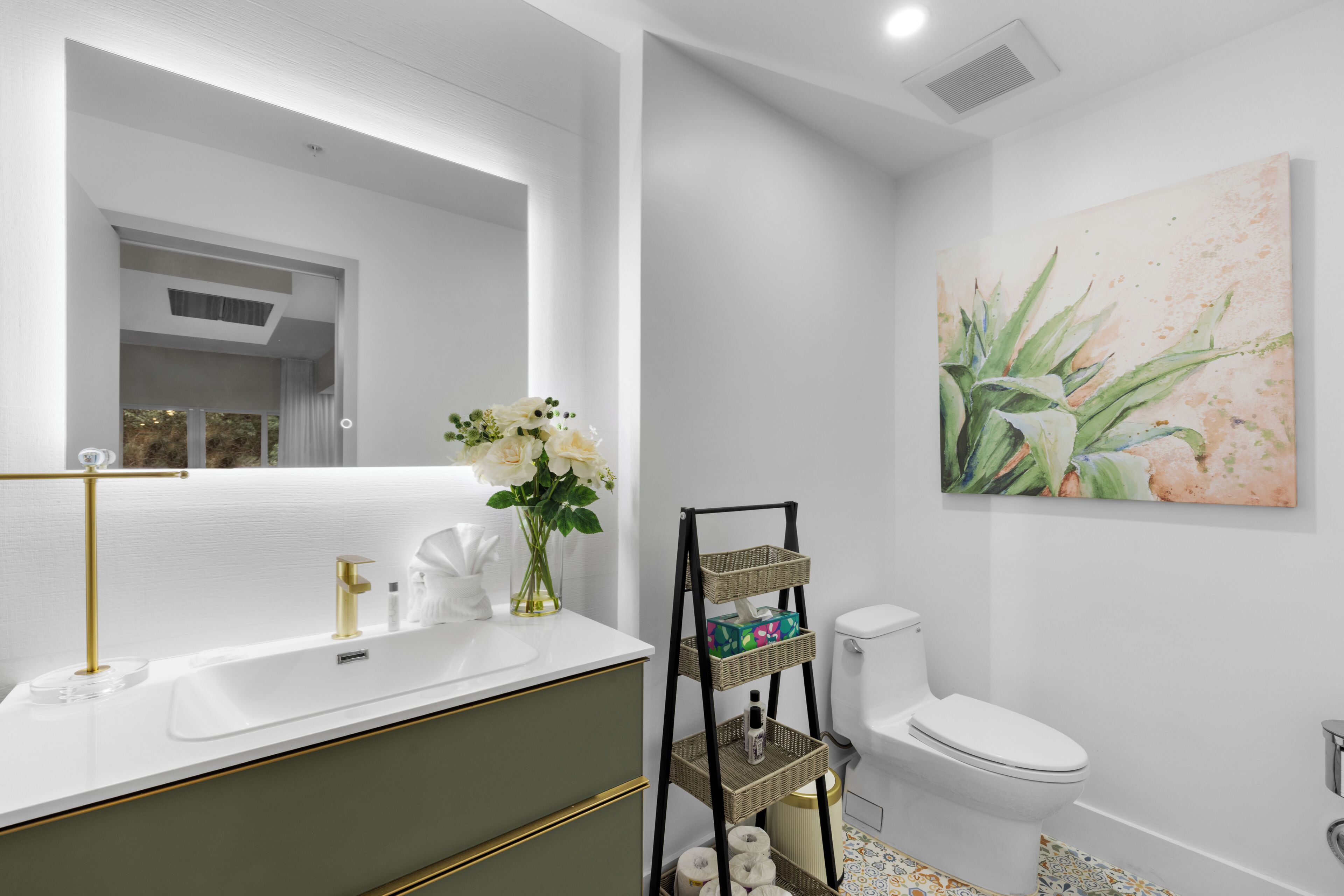 Un bany modern amb un lavabo blanc, detalls daurat i un vàter. Hi ha també un quadre penjat a la paret.
