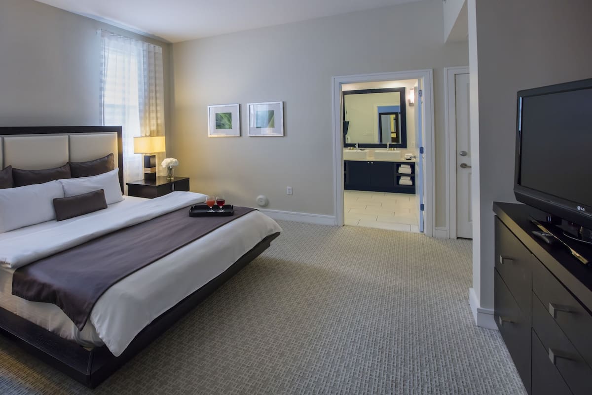 Une chambre d’hôtel avec un grand lit, une télévision, un bureau avec une lampe et une salle de bain visible à travers une porte ouverte.
