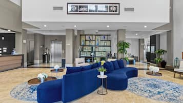 Un hall d’entrée spacieux, avec un canapé d’angle bleu, un comptoir de réception et un mur décoratif orné d’œuvres d’art encadrées.