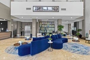 Un vestíbulo espacioso con un sofá seccional azul, un mostrador de recepción y una pared decorativa con obras de arte enmarcadas.
